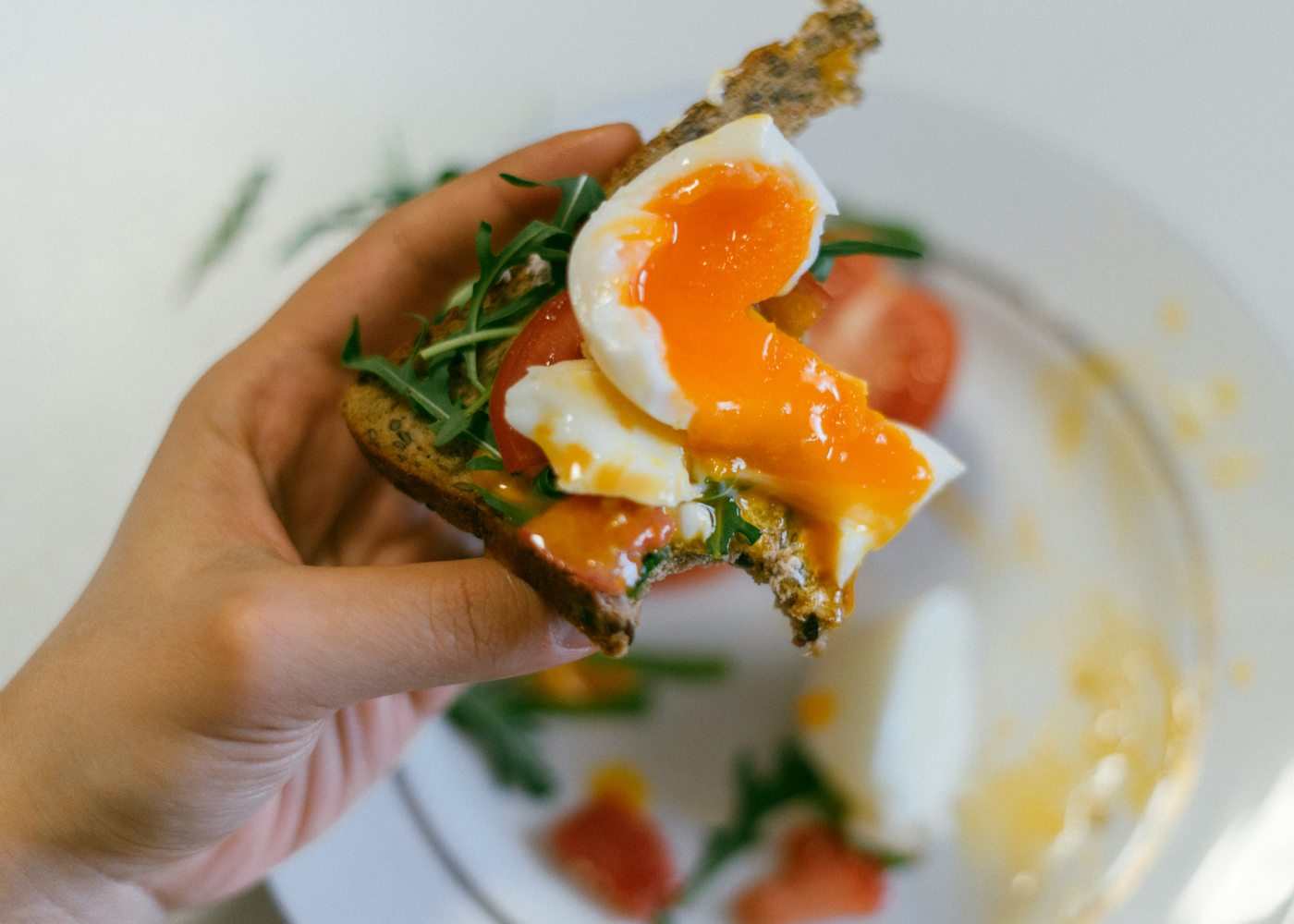 Hand holding avocado toast topped with a jammy egg